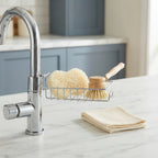 A modern sink caddy organizer holding a dry sponge and brush on a kitchen countertop next to a faucet.